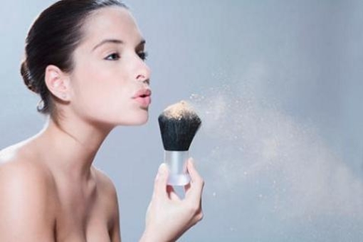 Young woman blowing powder from make-up brush, close-up, side view